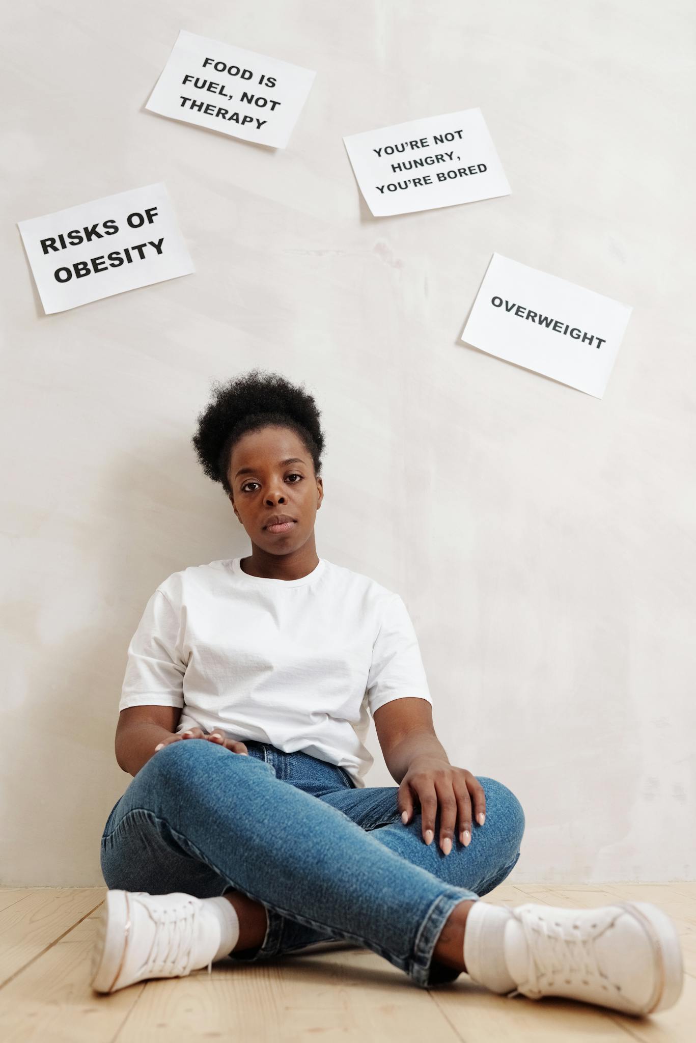 Woman sitting against wall with health-related slogans about obesity and nutrition.